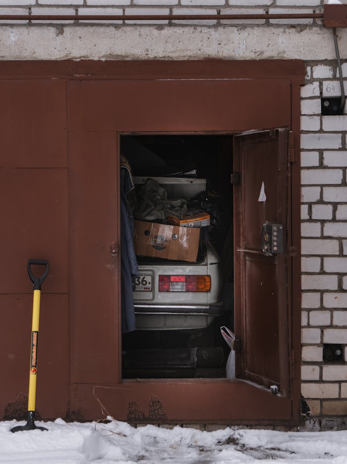 An open garage door reveals a forgotten car surrounded by snow and urban decay.